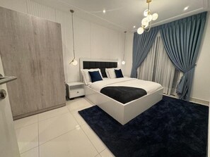 A modern bedroom with a large bed, bedside tables, a wardrobe, and a chandelier. - Loxwood House by Cozy (Accra)