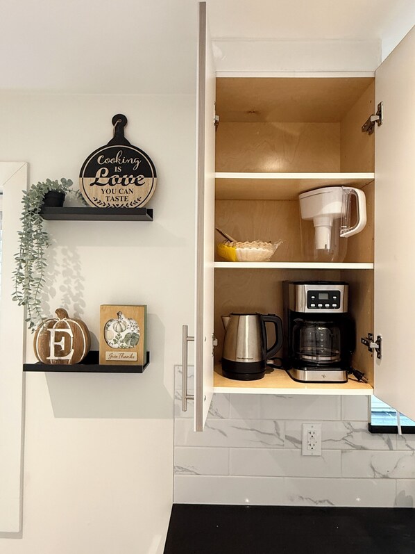 A kitchen with a wooden cabinet, a coffee maker, a kettle, and a sign that says 'Cooking is Love'.