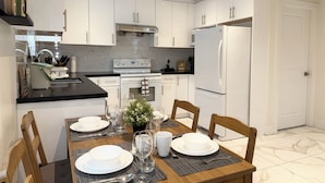 Une cuisine moderne avec des meubles blancs, un plan de travail noir et une table à manger pour quatre personnes.