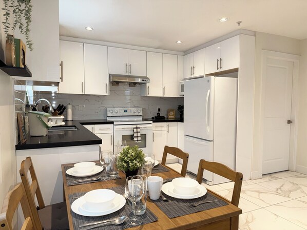 Una cocina moderna con armarios blancos, encimera negra y una mesa de comedor preparada para cuatro.