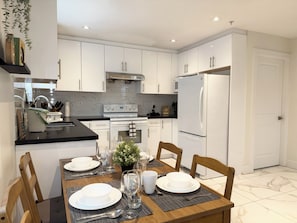 Una cocina moderna con armarios blancos, encimera negra y una mesa de comedor preparada para cuatro.