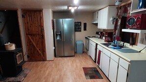 A kitchen with wooden flooring, a stainless steel refrigerator, a blue trash bin, and white cabinets.