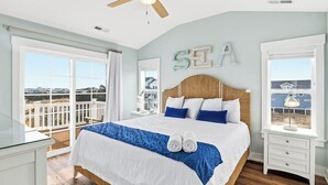A bedroom with a large bed, a ceiling fan, and a view of the sea through large windows. - Summer Moon | 1,615 ft to the beach | Private Pool, Hot Tub, and Dog Friendly (Corolla)
