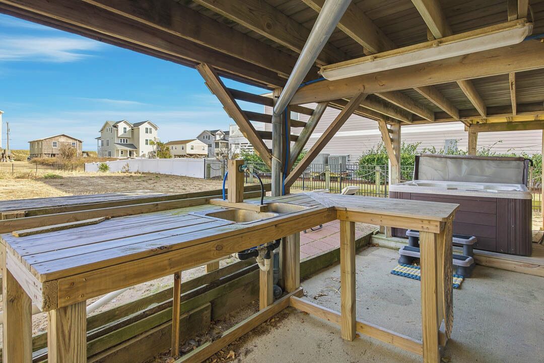 A wooden deck with a hot tub and a wooden table, overlooking a residential area.