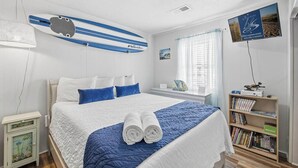 Ein ordentlich eingerichtetes Schlafzimmer mit einem Bett, einem Bücherregal und einer Surfbrett-Dekoration an der Wand.