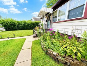A residential house with a stone retaining wall, a front porch, and a well-maintained lawn. - Spacious, Charming 4BR, 2BA Glen Burnie Home, Sleeps 9 (Glen Burnie)