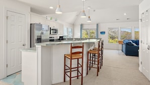 Une cuisine moderne avec des meubles blancs, un îlot central doté de tabourets et un éclairage suspendu.