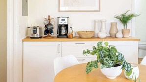 Une cuisine moderne avec des meubles blancs, un plan de travail en bois, une machine à café et une plante en pot posée sur la table.