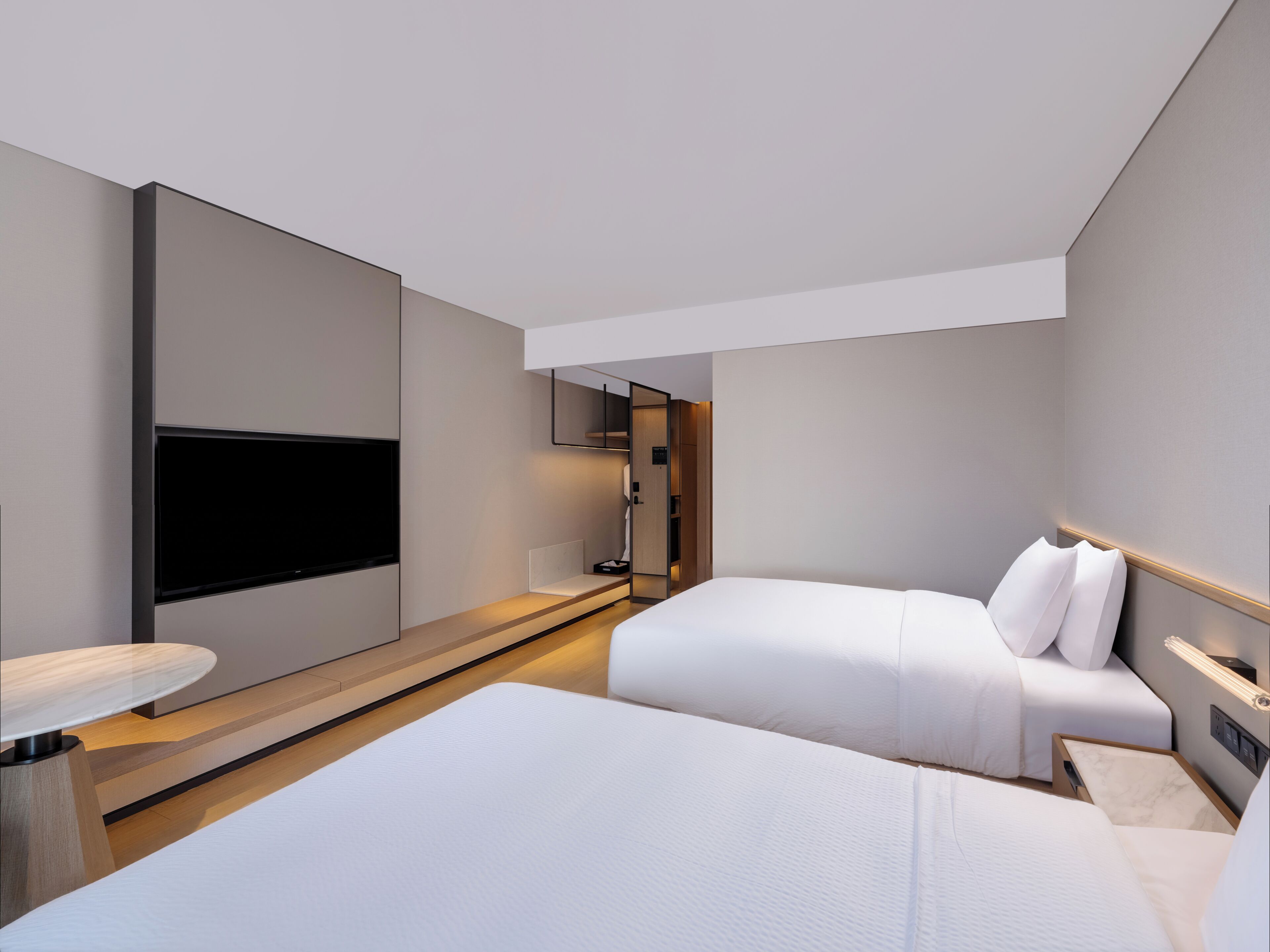 A modern hotel room with a large flat-screen TV, a bed, a bedside table, and a small desk area.