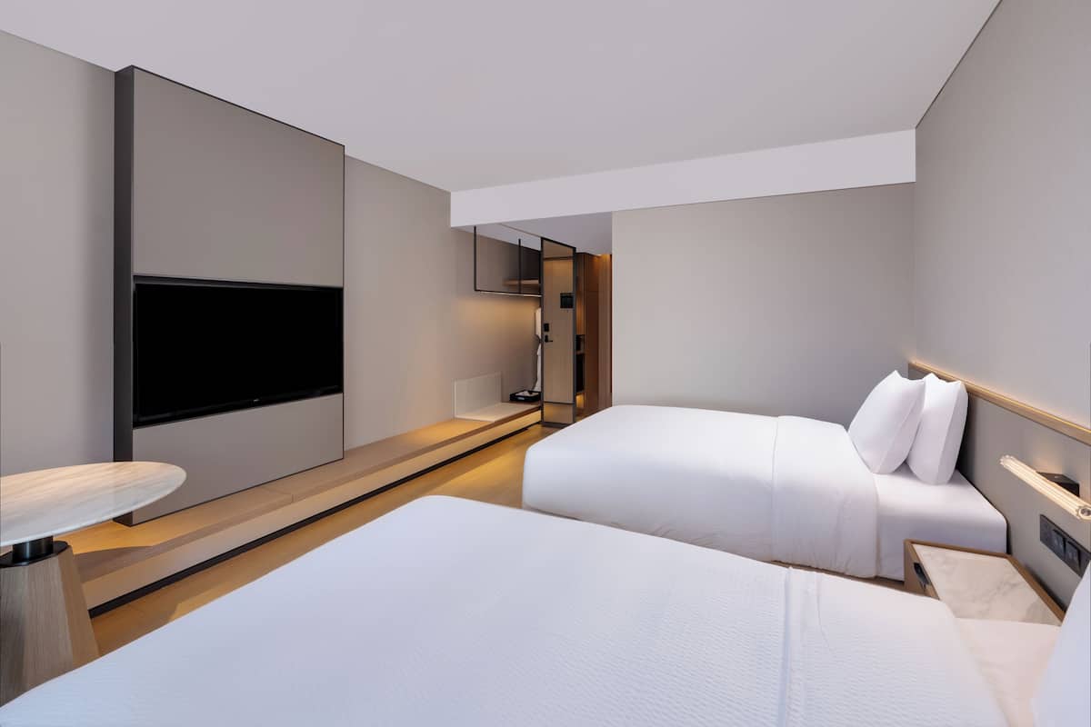 A modern hotel room with a large flat-screen TV, a bed, a bedside table, and a small desk area.