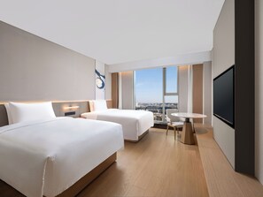 Habitación de hotel moderna con dos camas, una mesita, un televisor y vistas a la ciudad.