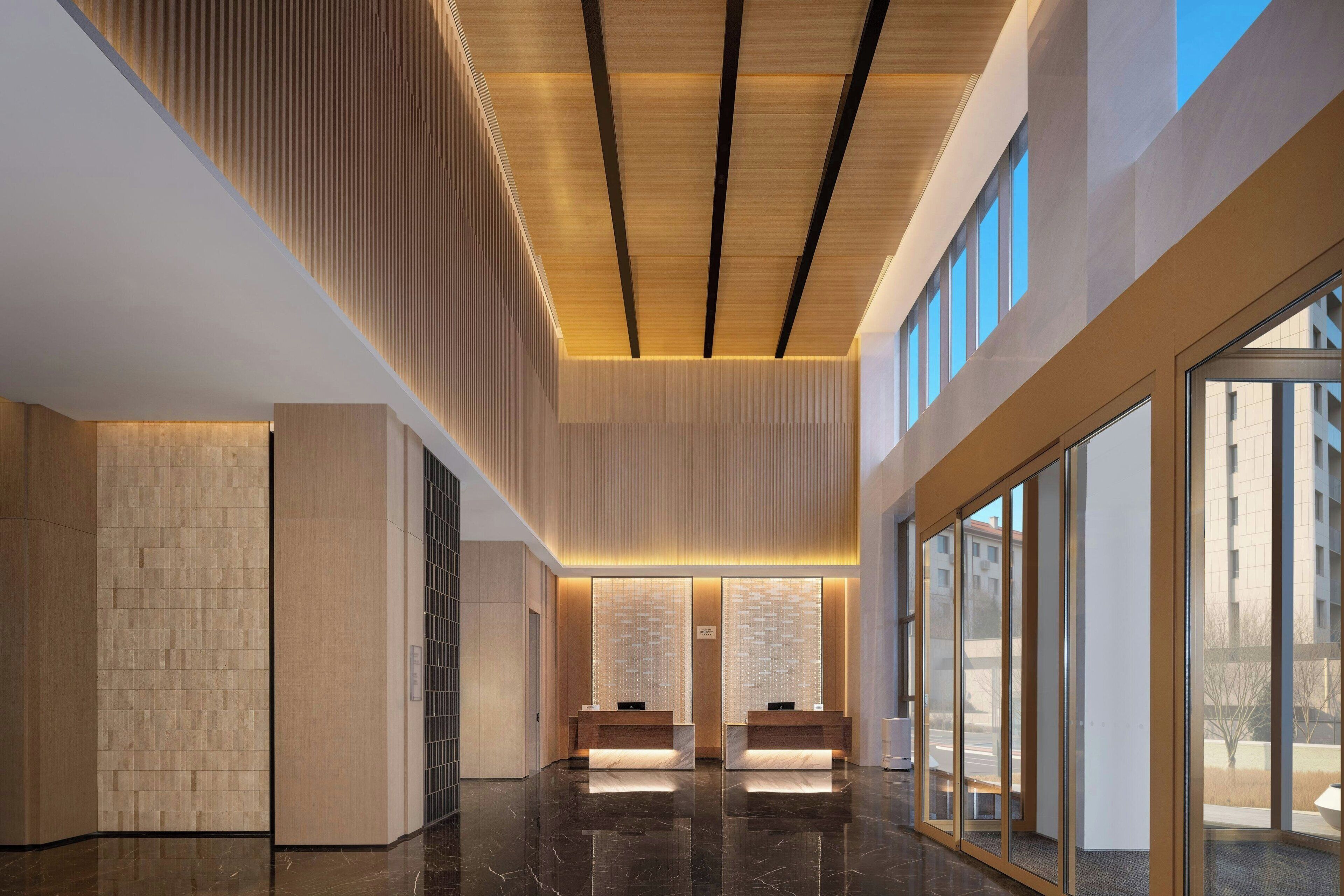 A modern lobby with a wooden ceiling, glass walls, and a marble floor.