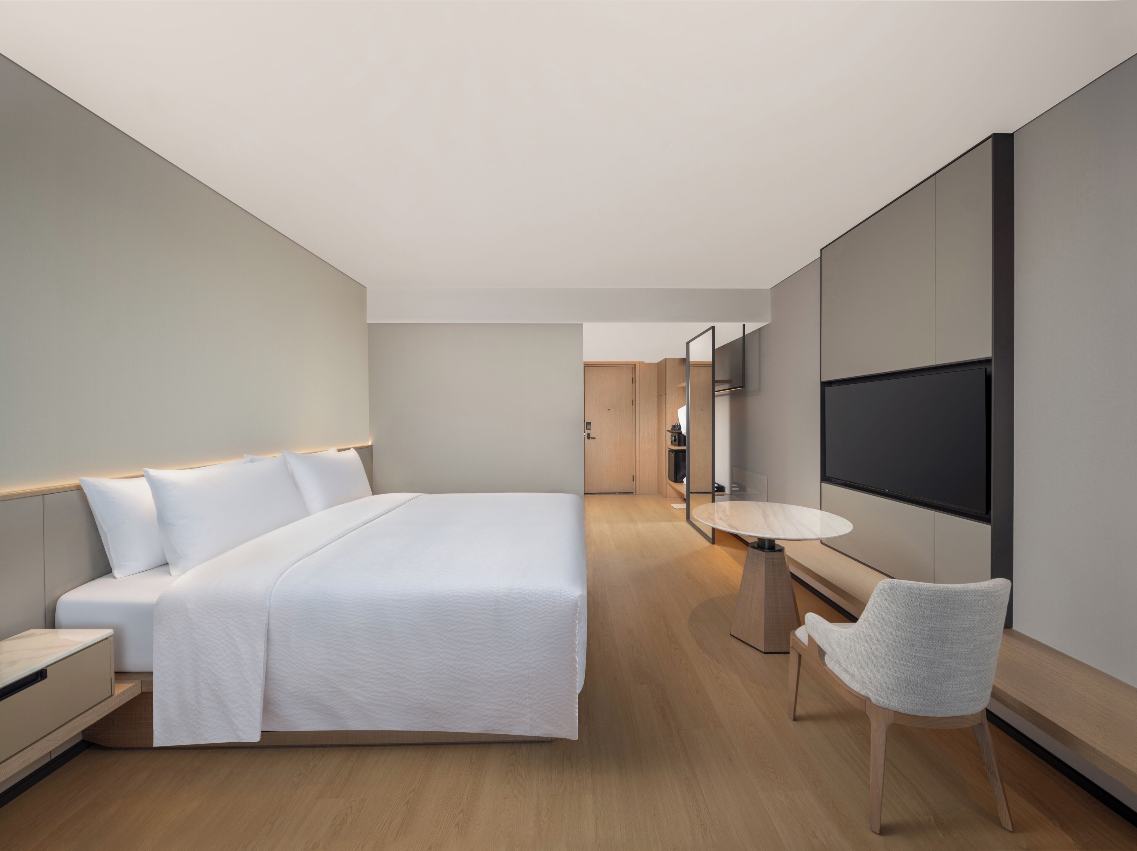 Una habitación de hotel moderna con una cama grande, una mesita redonda pequeña, una silla y un televisor fijado a la pared.