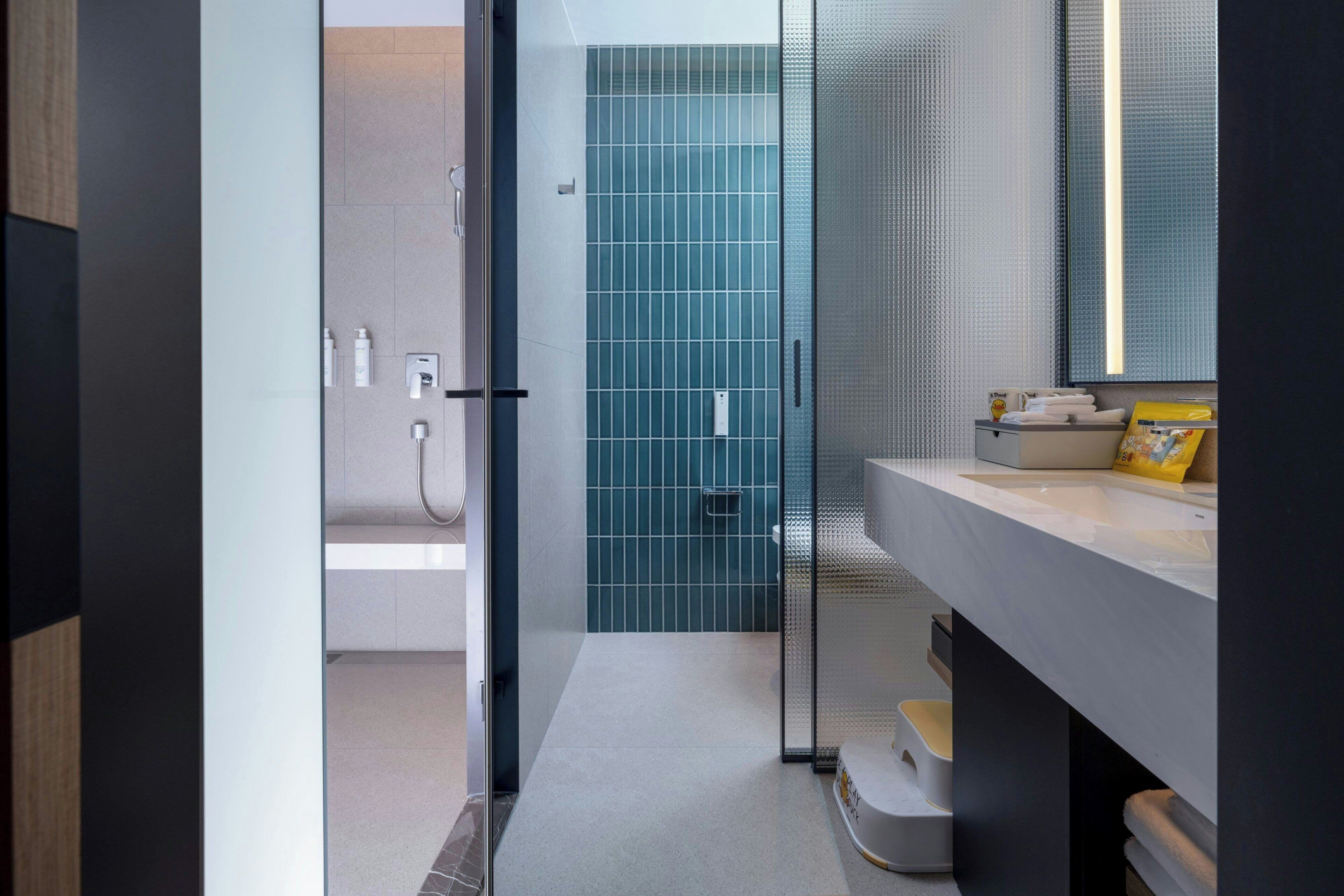 Un baño moderno con cabina de ducha de vidrio, un lavamanos blanco y un espejo, y un revestimiento de azulejos en la pared de la ducha.