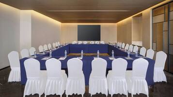Un salón de conferencias con una larga mesa, sillas blancas y botellas de agua.