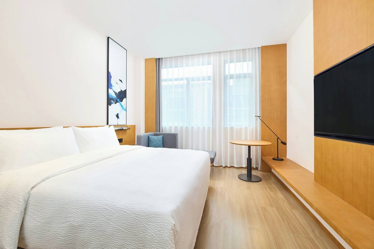 A hotel room with a large bed, a desk with a chair, a TV, and a window with curtains.