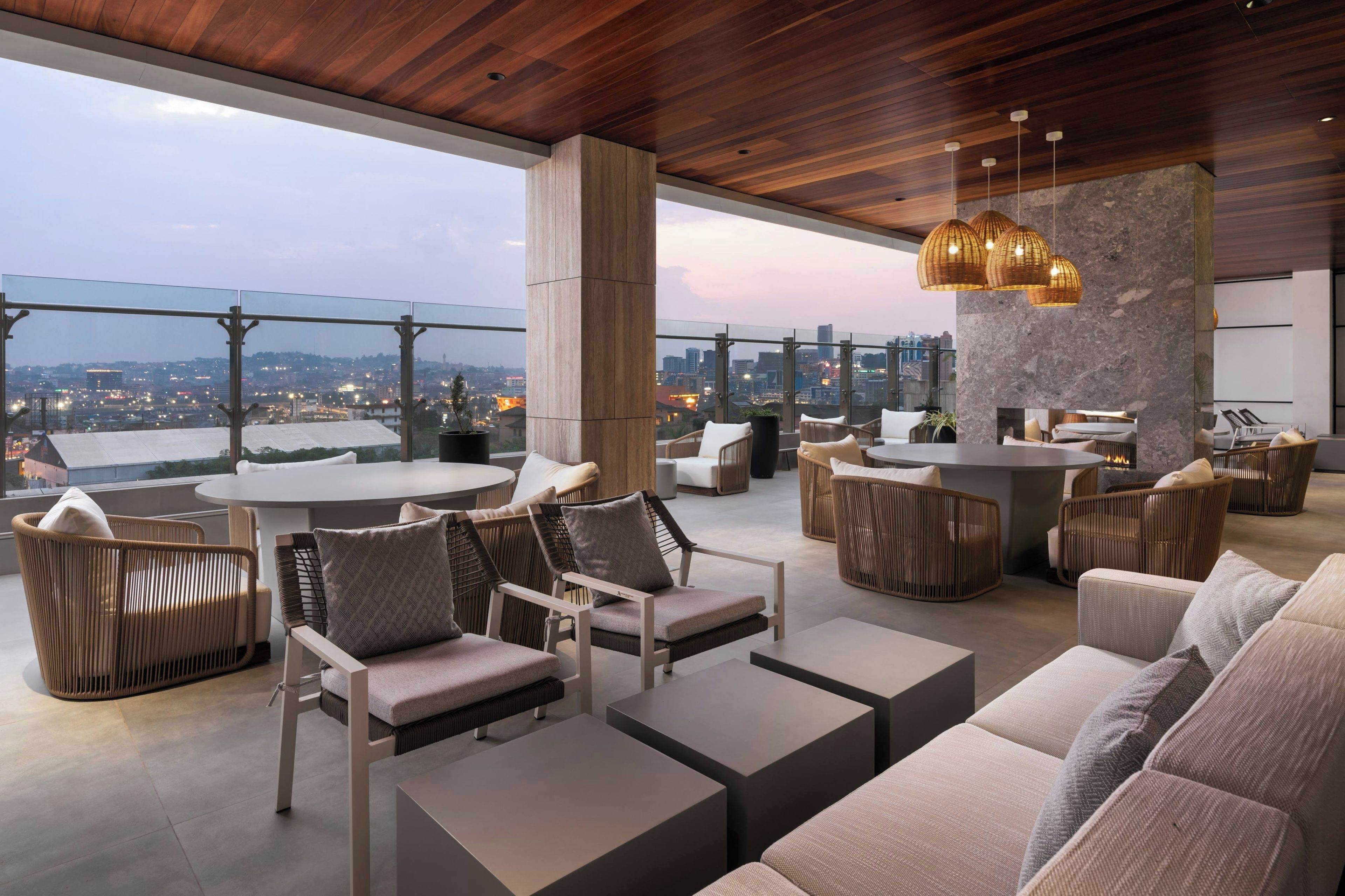 A modern outdoor lounge area with seating arrangements, a round table, and a view of the cityscape.