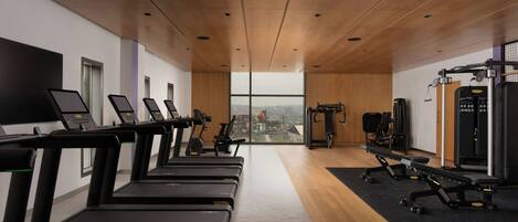 A gym with treadmills, weight machines, and a large window offering a city view.