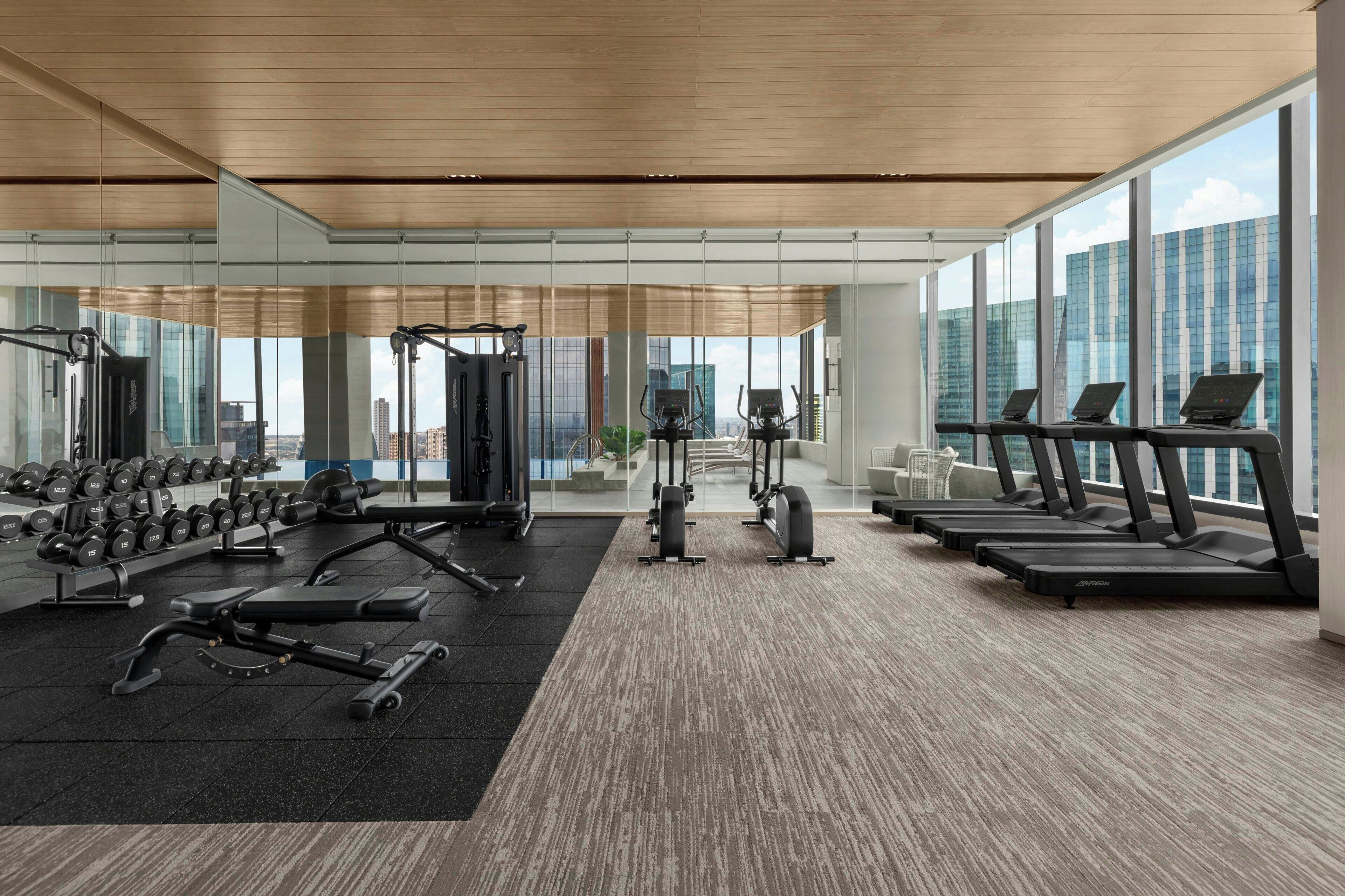 A modern gym with cardio equipment, weight machines, and dumbbells.