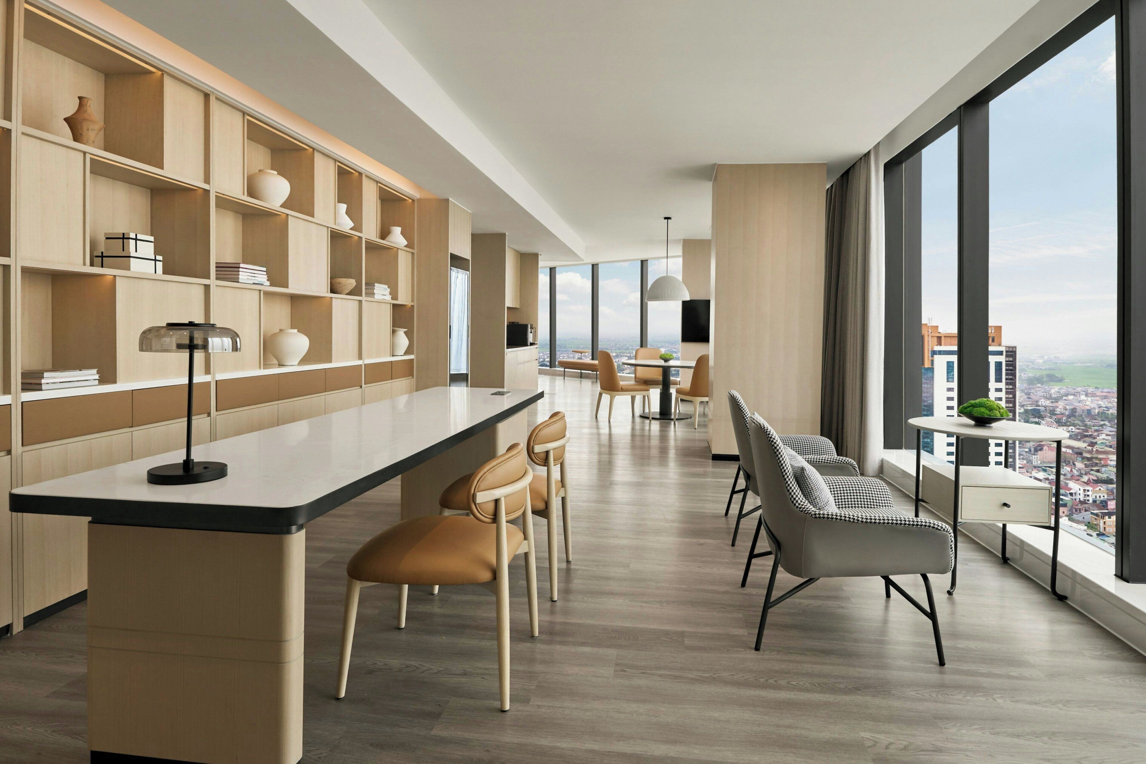 A modern kitchen with a central island, dining area with chairs, and large windows offering a city view.