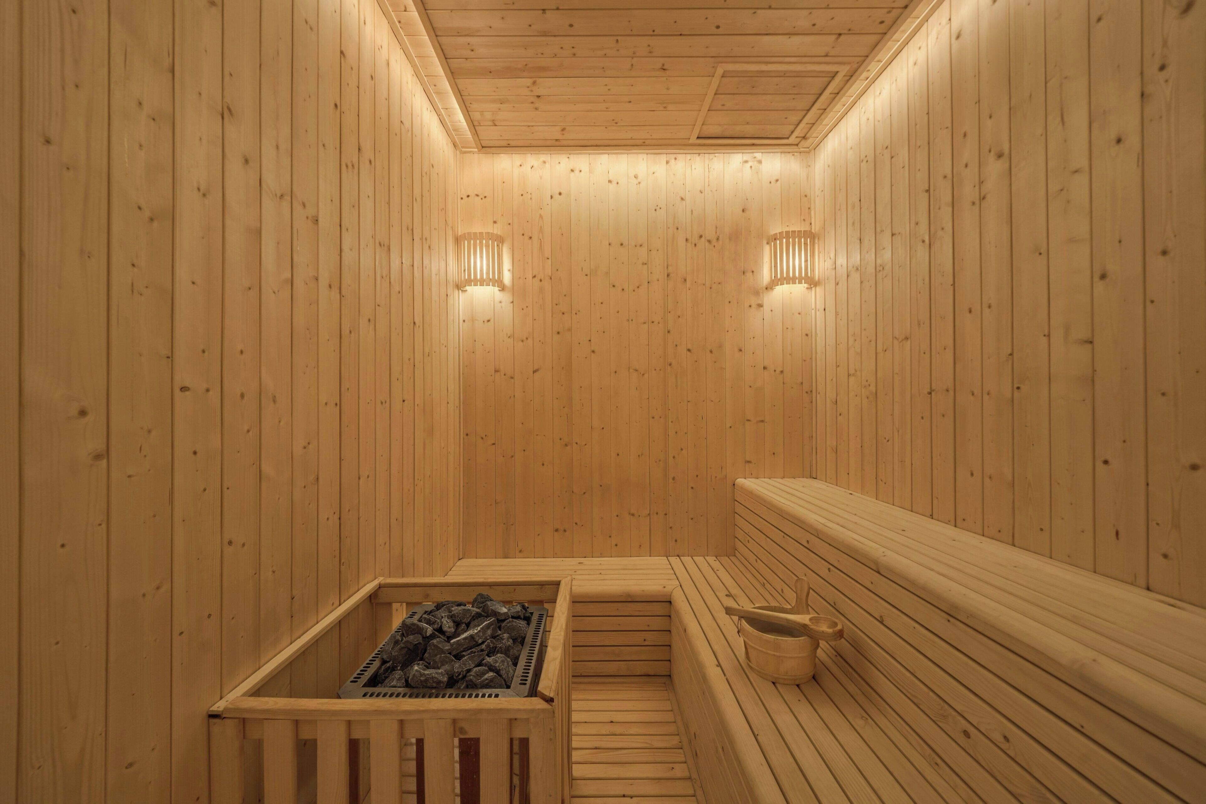 A wooden sauna with benches, a heated floor, and wall-mounted lights.
