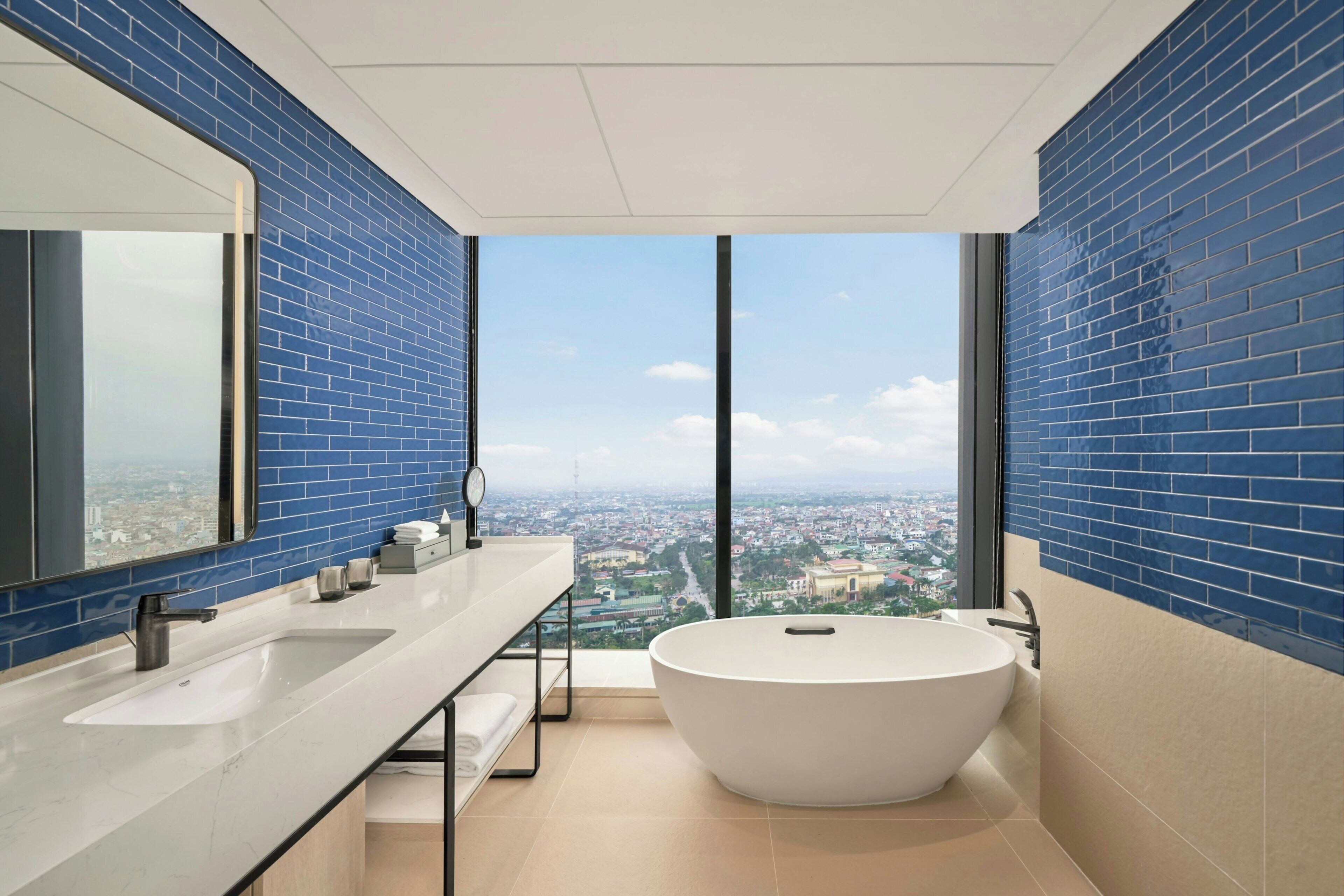 A modern bathroom with a large bathtub, dual sinks, and a city view through large windows.