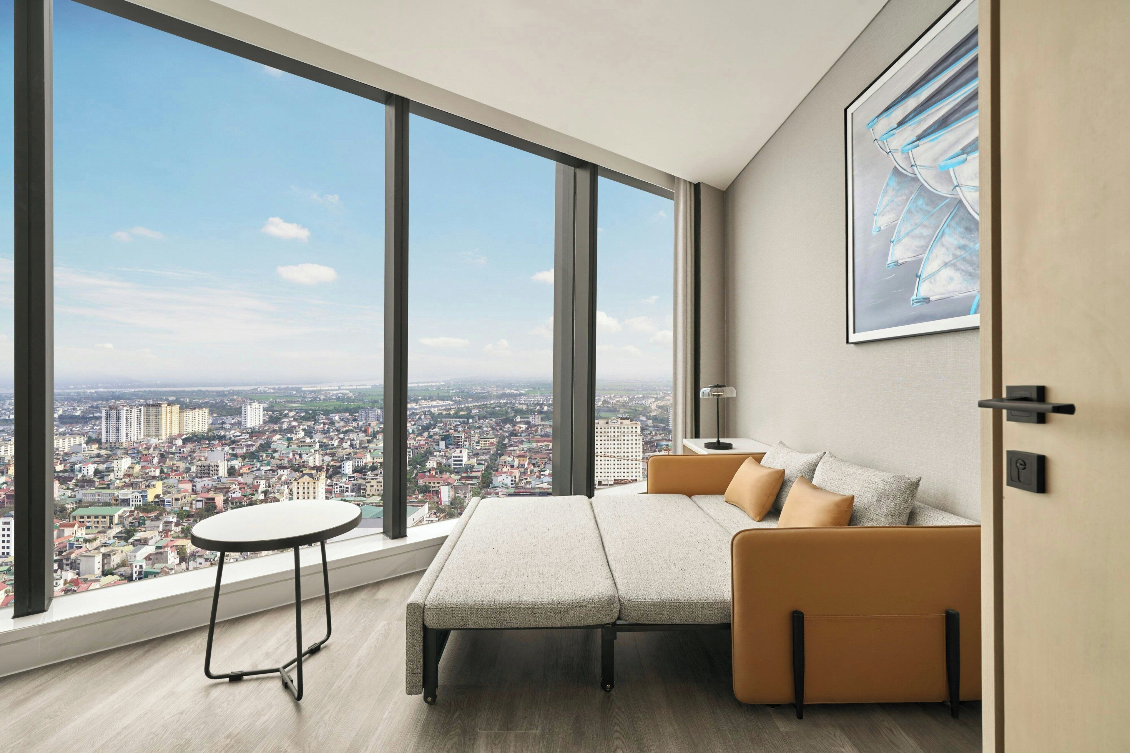 A modern room with a large window, a sofa, a small table, and a framed picture on the wall.