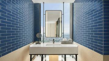 Ein Badezimmer mit blauen Ziegelwänden, einem weißen Waschbecken, einem Spiegel und Blick auf die Stadt.