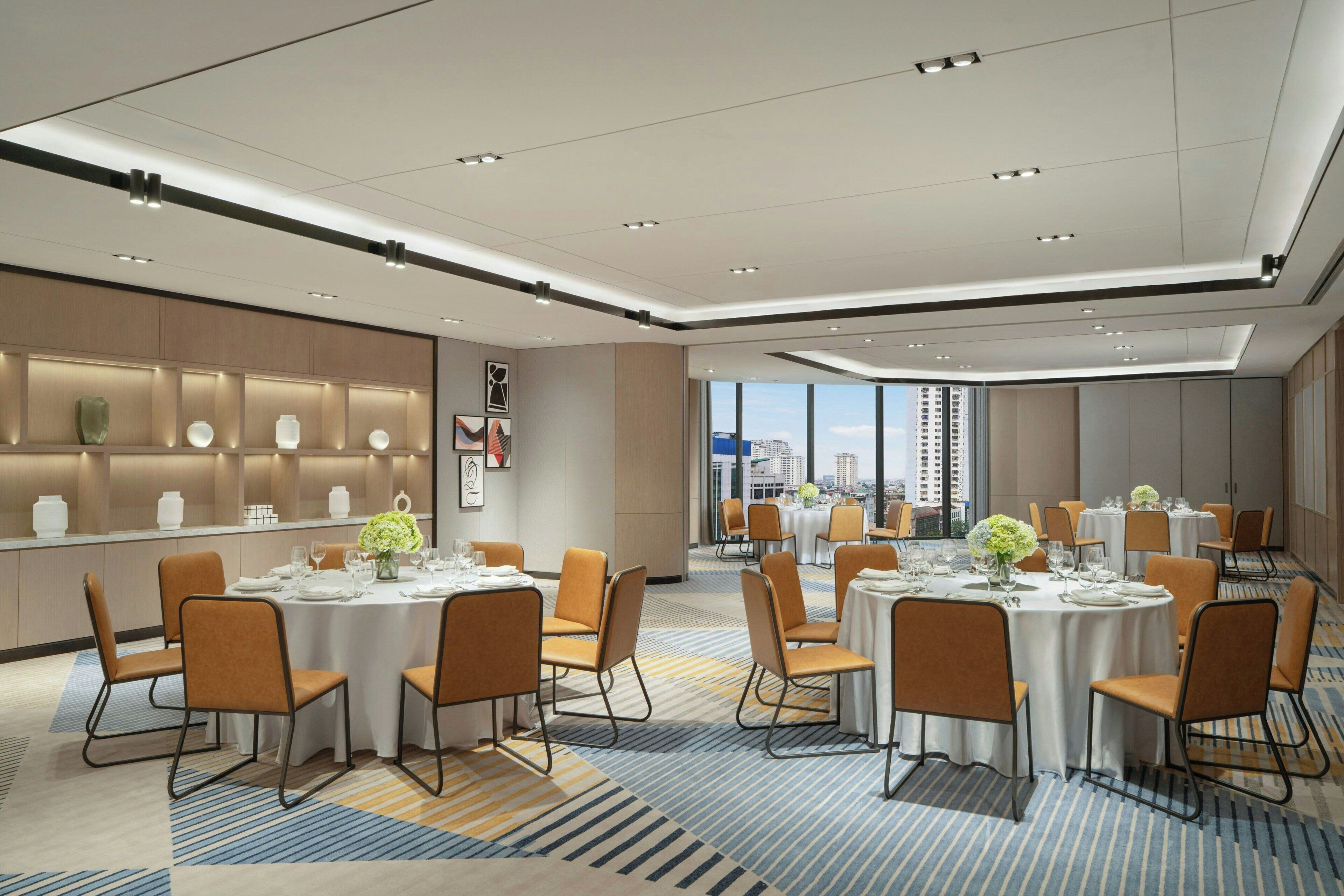 Een modern restaurantgedeelte in een hotel met ronde tafels, oranje stoelen en uitzicht op de stad.