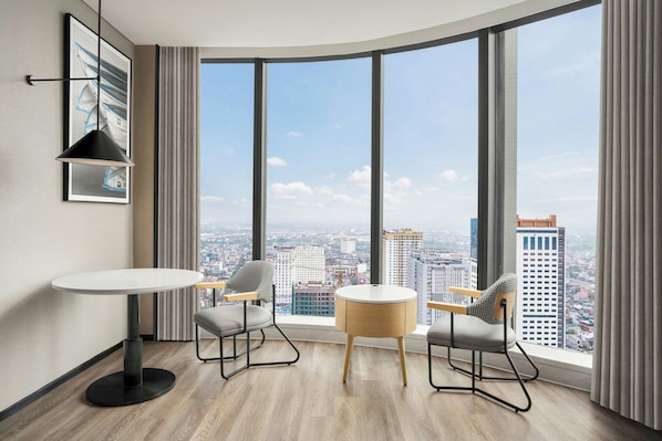 Une pièce moderne avec une fenêtre incurvée, deux chaises, une petite table et un tableau encadré au mur.
