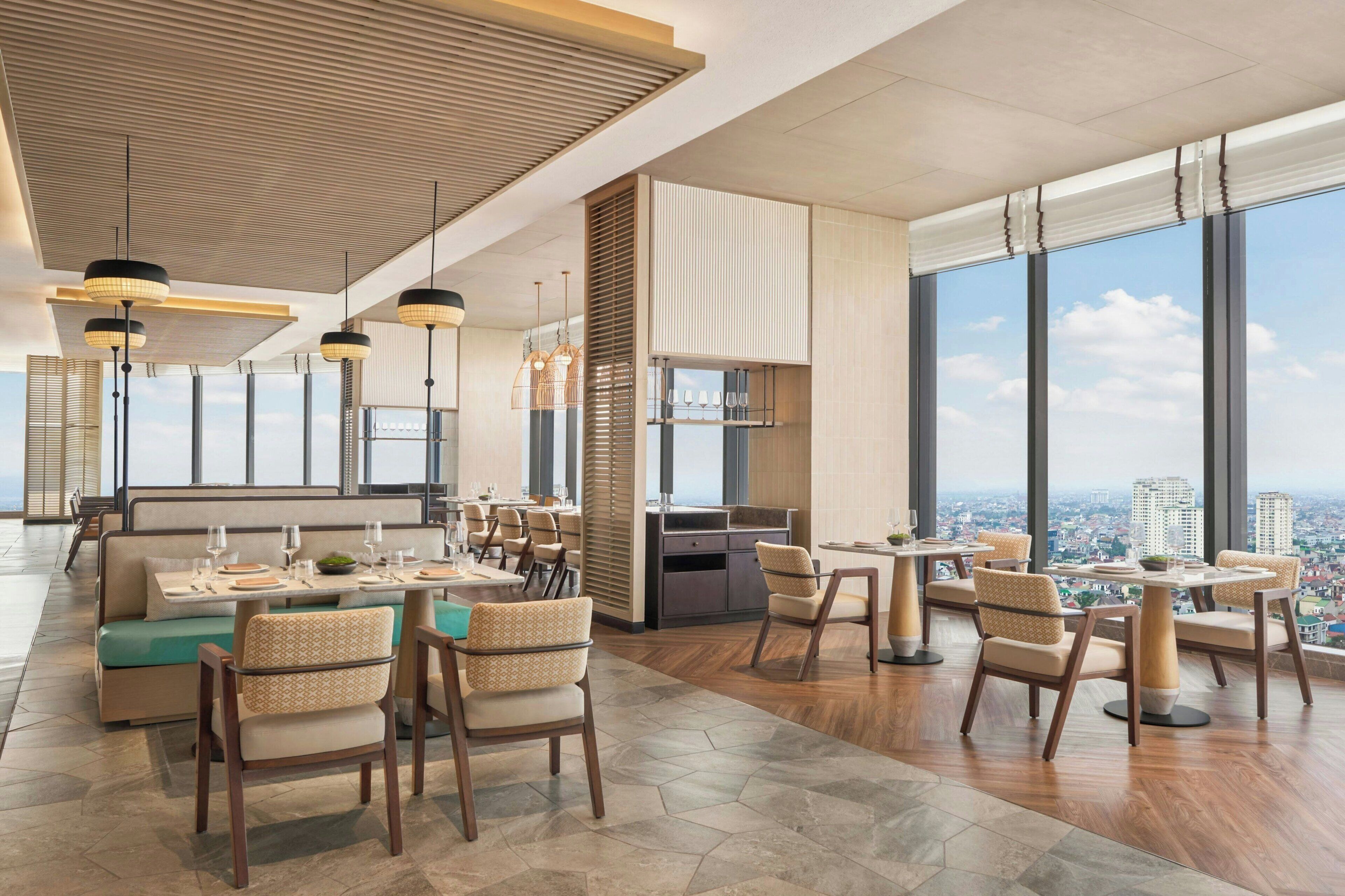 A modern restaurant with high ceilings, large windows, and a city view.