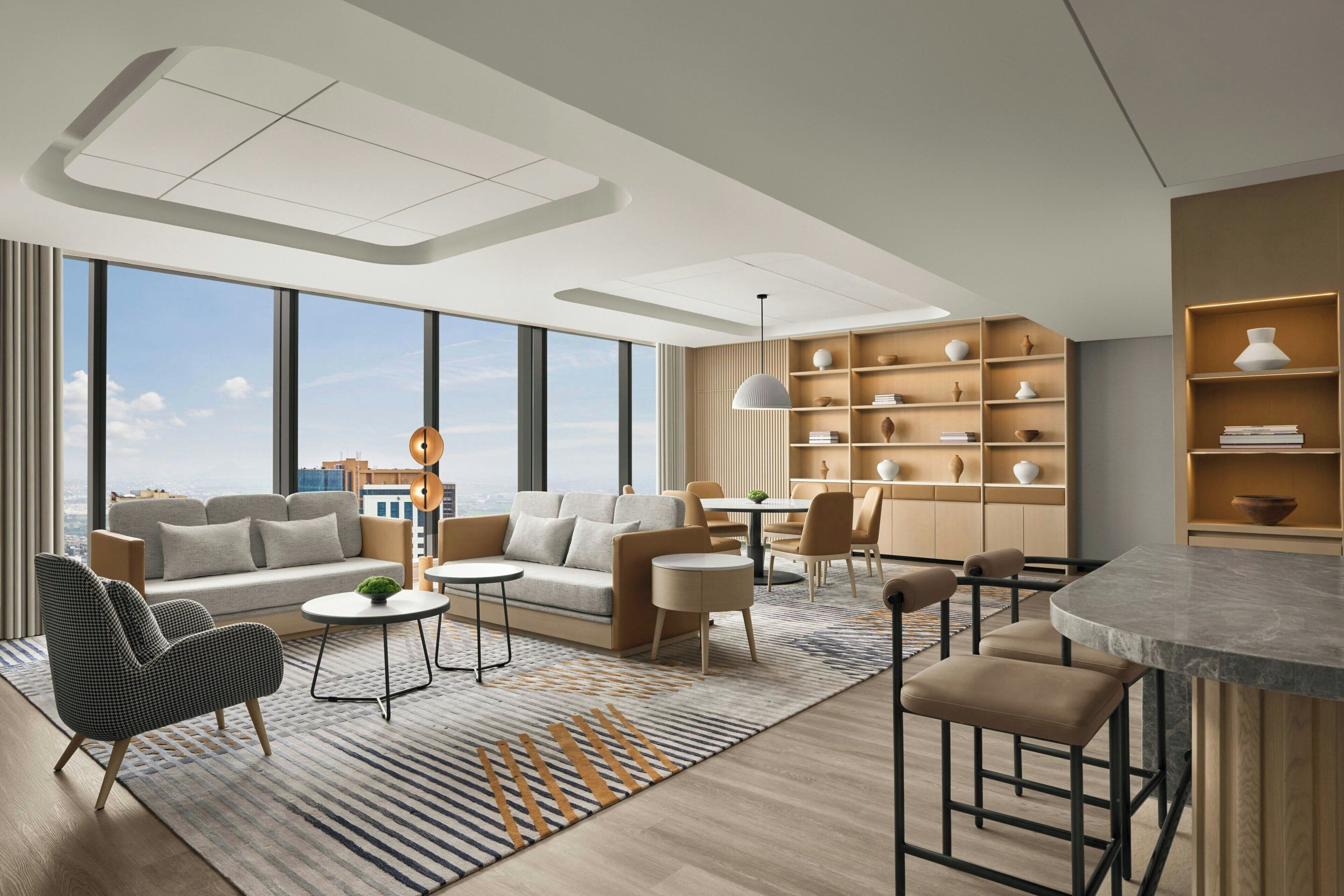 A modern living room with a sofa, chairs, a coffee table, and a dining area with a table and chairs. There is a large window providing a view of the city.