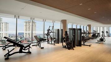 A modern gym with various exercise equipment, large windows, and a city view.