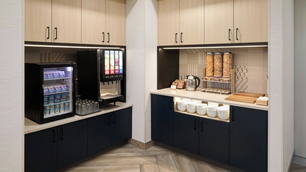 A hotel kitchenette with a refrigerator stocked with beverages, a coffee machine, and a coffee station with cups and a kettle. - Towneplace Suites By Marriott Montreal Airport (Dorval)