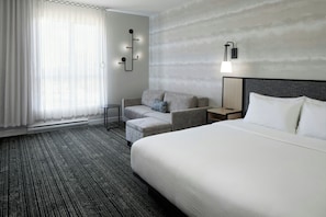 Una habitación de hotel con una cama grande, un sofá, una mesita y una lámpara de pared.