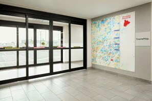 A modern interior with large glass doors leading to a parking area, a colorful map on the wall, and a sign indicating 'Bienvenue à Montréal, QC'. - Towneplace Suites By Marriott Montreal Airport (Dorval)
