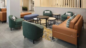 A modern lounge area with green and brown upholstered seating, a patterned rug, and a wooden partition with vertical slats. - Towneplace Suites By Marriott Montreal Airport (Dorval)