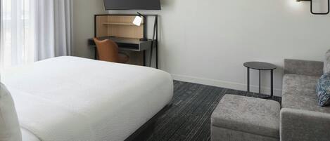 Una habitación de hotel con cama, escritorio, silla, televisor y una mesita.