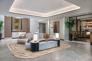 Un hall d’hôtel moderne avec un espace salon aux lignes courbes, un sol en marbre et un luminaire central.