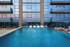 Et moderne hotel med poolområde, liggestole og udsigt over bybilledet.