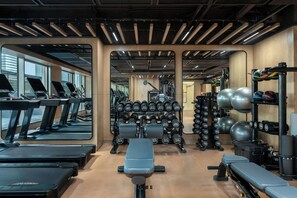 Une salle de sport équipée de tapis de course, de bancs de musculation, d’haltères et de ballons d’exercice.