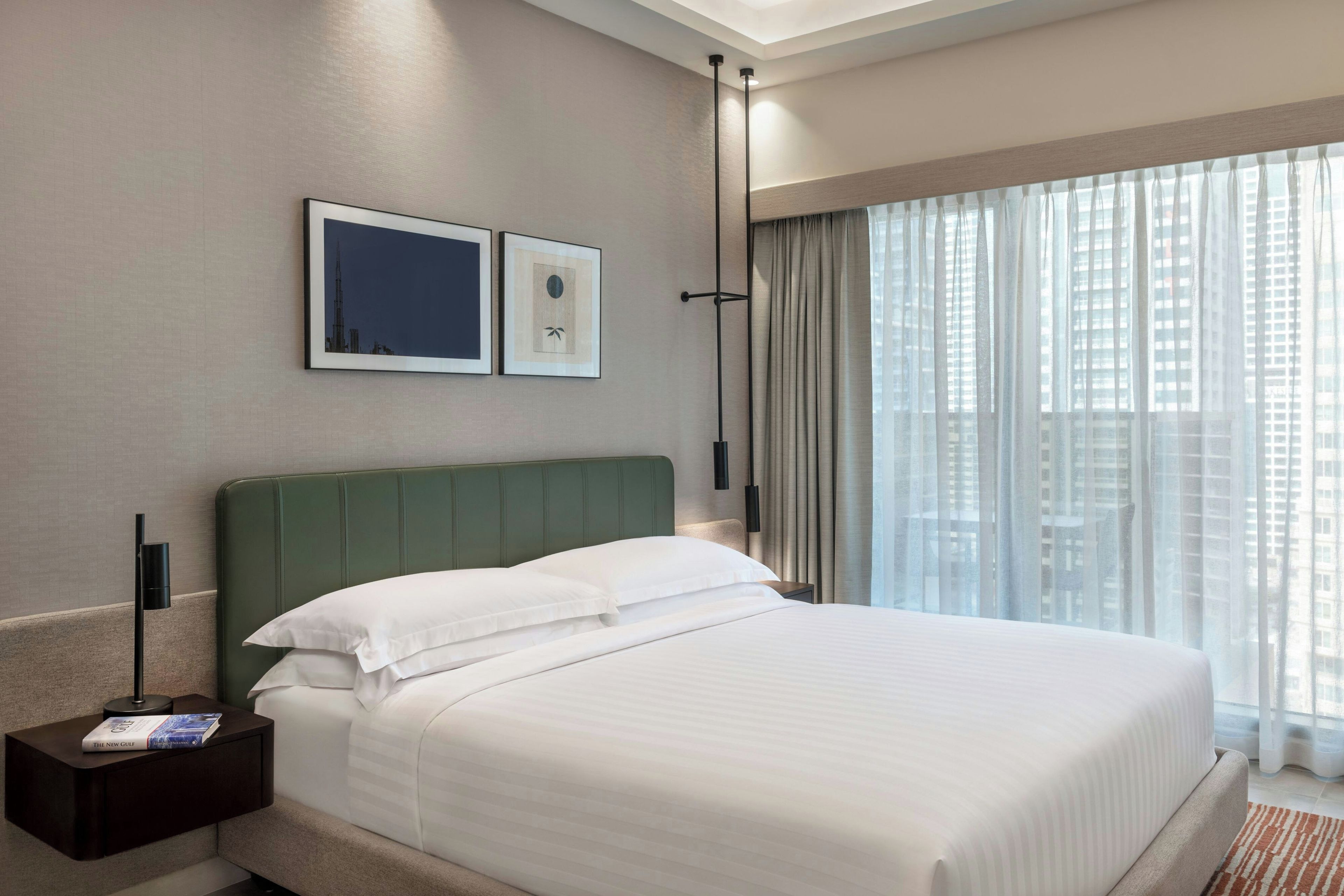 Habitació d'hotel amb un llit, una tauleta de nit, un quadre amb marc i una finestra amb cortines.