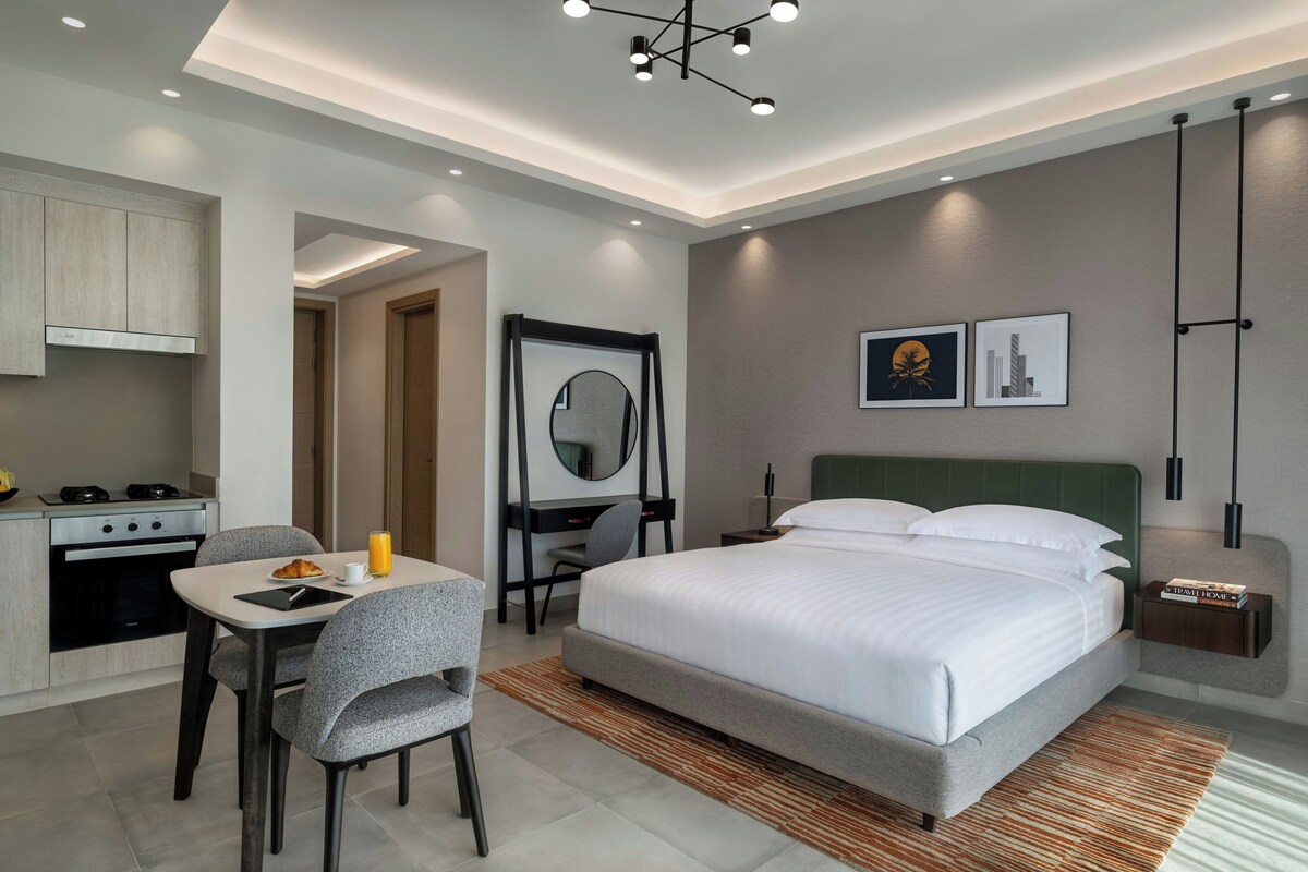Una habitación de hotel moderna con una cama, mesita de noche, lámpara y vista a la ciudad.