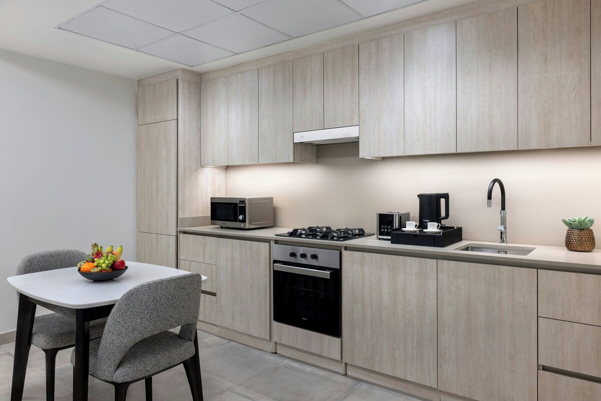 Una cocina moderna con armarios de madera clara, microondas, estufa y lavaplatos.