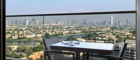 A balcony with a table and chairs, overlooking a cityscape with buildings and a river.