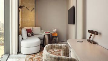 A modern hotel room with a sofa, a small round table, a chair, a desk, and a TV mounted on the wall.