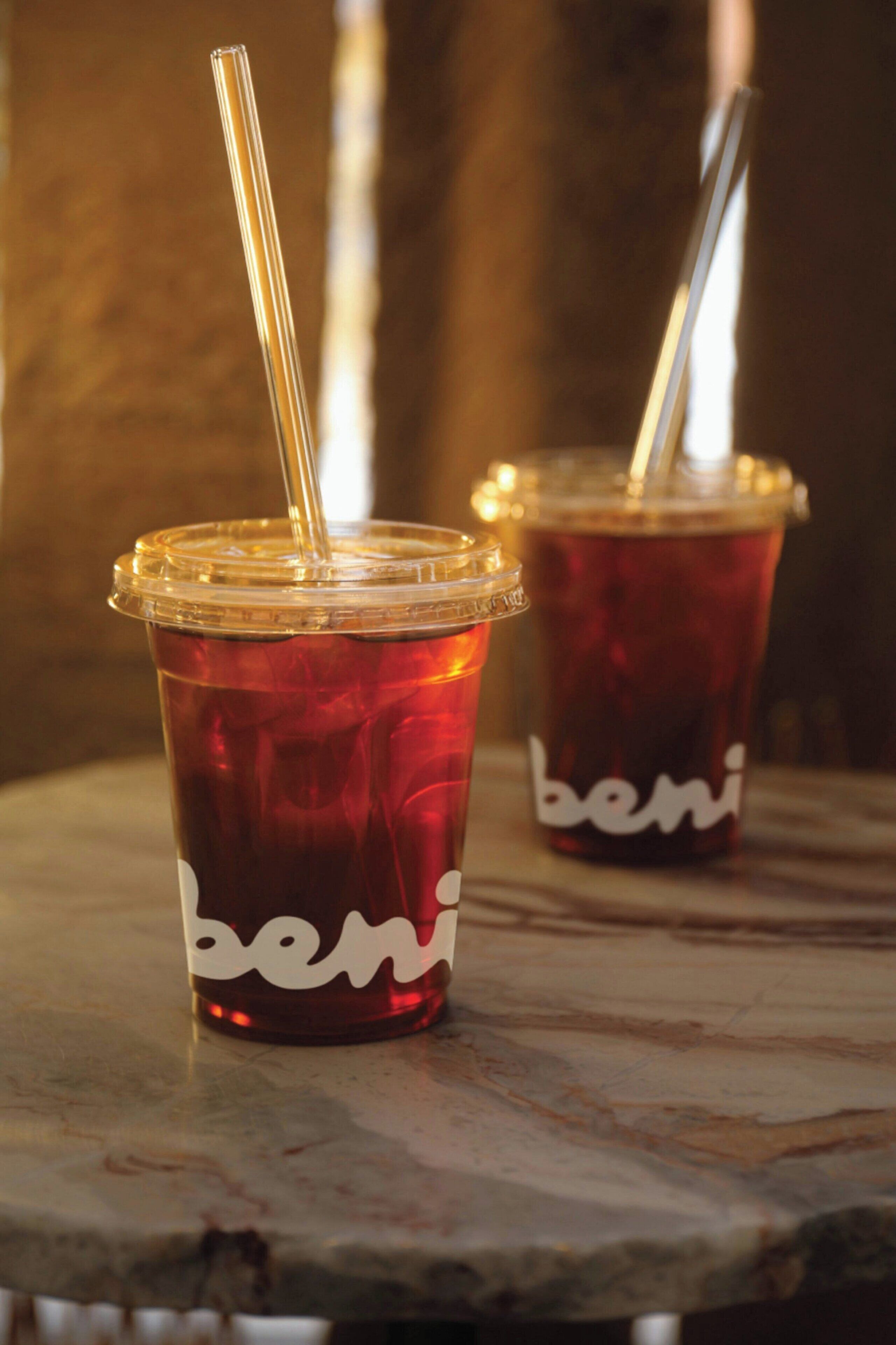 Two plastic cups with straws on a wooden surface.