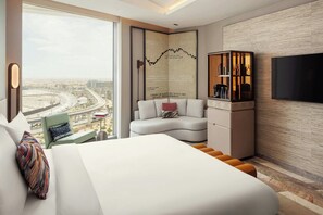A modern hotel room with a large bed, a sofa, a TV, and a city view.