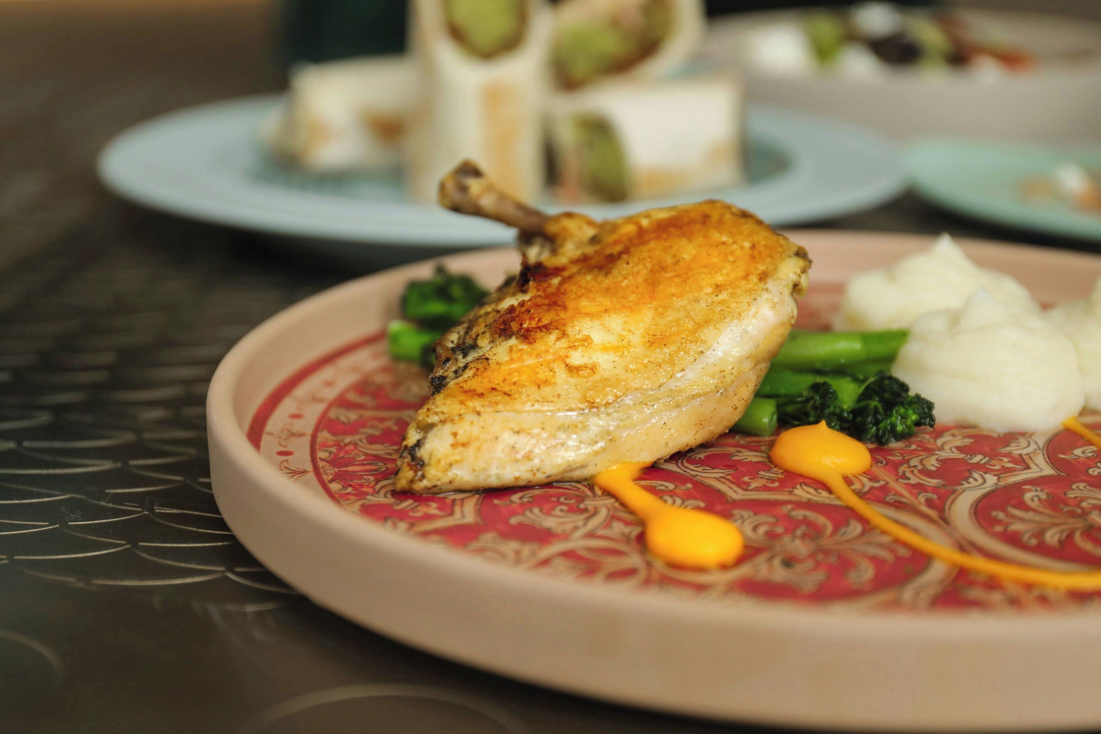 A plate with a roasted chicken leg, broccoli, and a dollop of sauce.