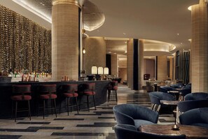A modern bar area with a curved counter, multiple bar stools, and a seating area with sofas and tables. - W Riyadh - KAFD (Riyadh)